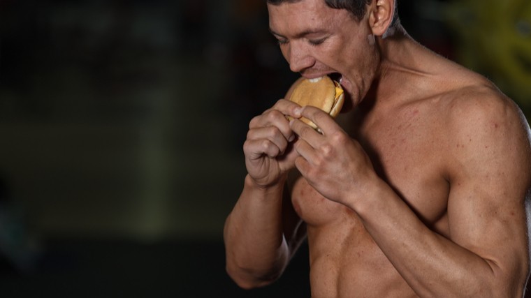 Muscular man eating cheeseburger
